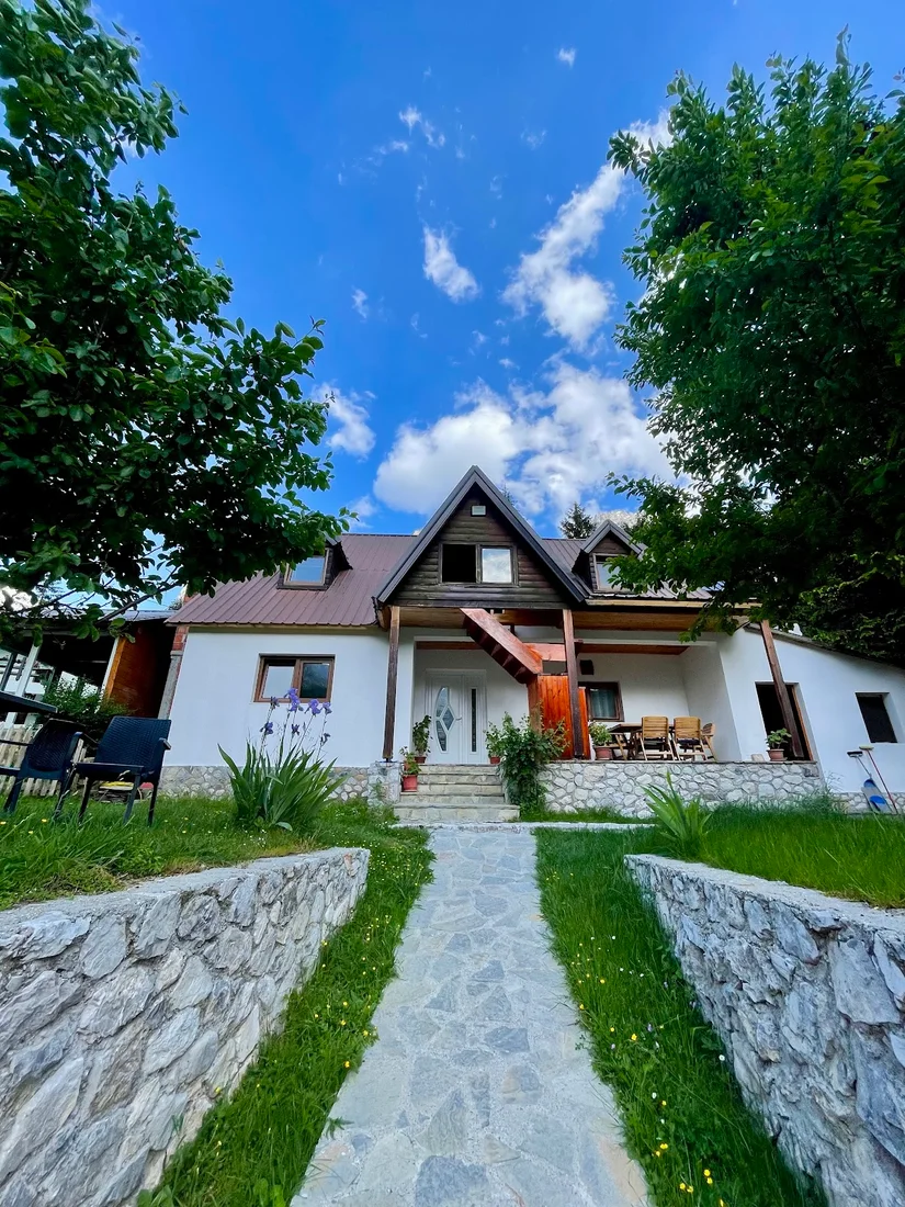 White gabled guesthouse with a stone garden and flagstone path at Bujtina Albjoni in Valbona