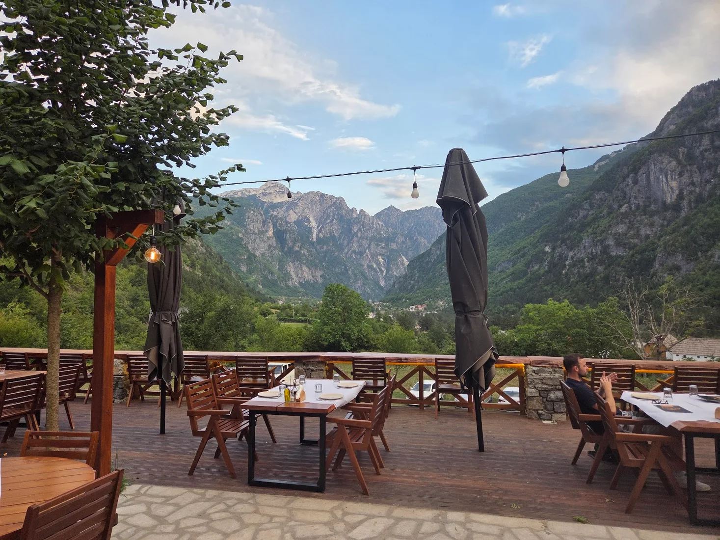 Wooden deck terrace with set tables opening onto the valley and peaks at Hotel Restaurant Alpet in Theth