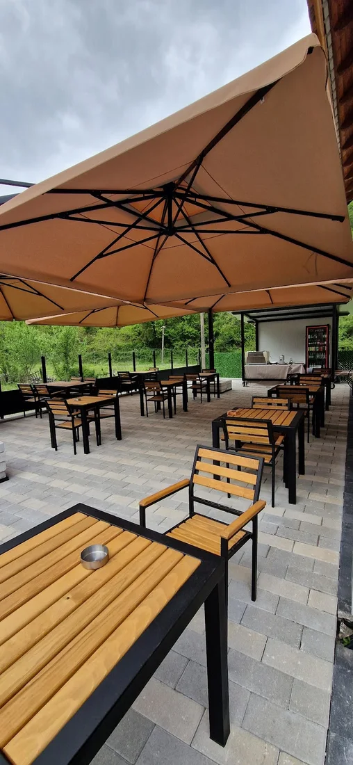 Paved garden terrace with wooden tables under large umbrellas at Bujtina Tinari in Fushë-Thethi