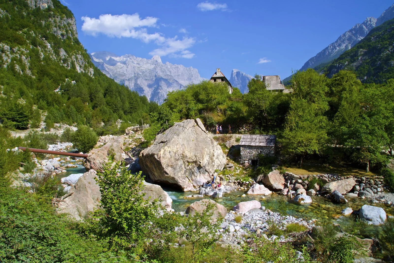 The Theth river running past a stone mill and houses below the grey peaks of the Accursed Mountains