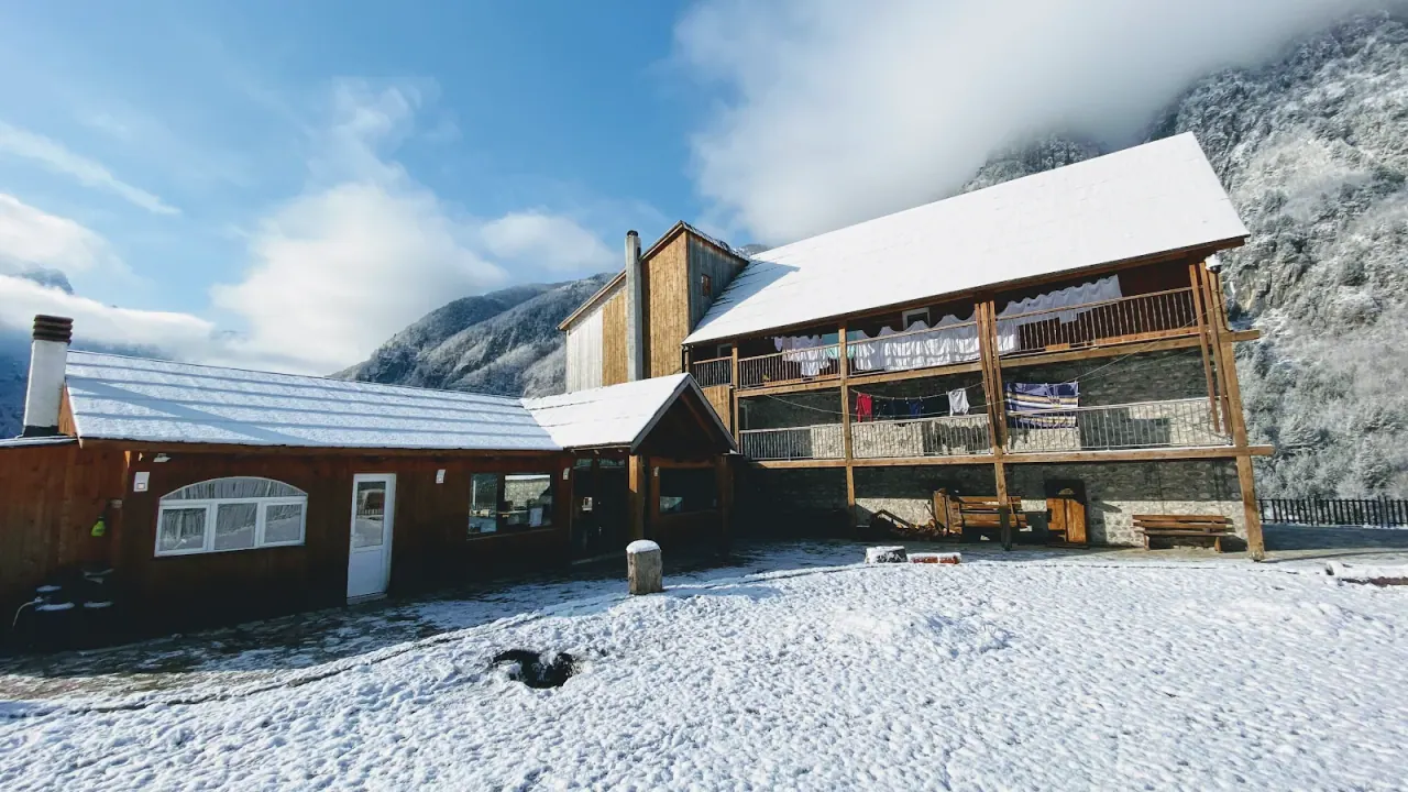 Timber and stone buildings of Bujtina Polia guesthouse below snow-covered peaks in Theth