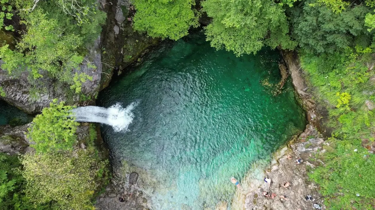 Aerial view of the blue-green Blue Eye pool of Theth with a waterfall feeding it