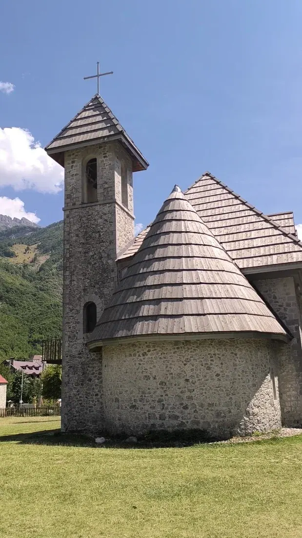 Side view of the Theth stone church showing the bell tower and shingled conical roof