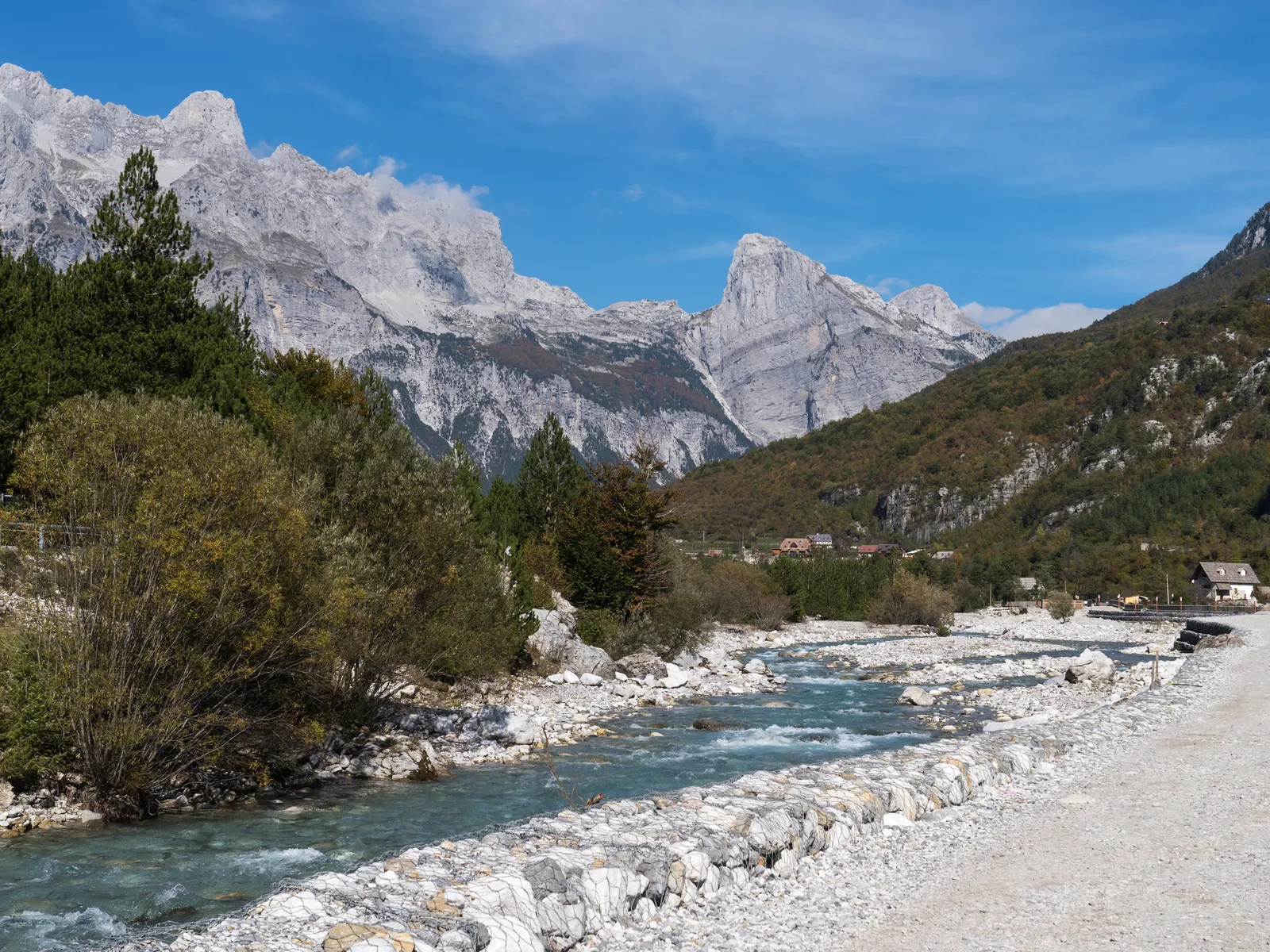 The Theth river running over a bed of white limestone below the bare grey peaks of the Albanian Alps, a gravel track along the near bank