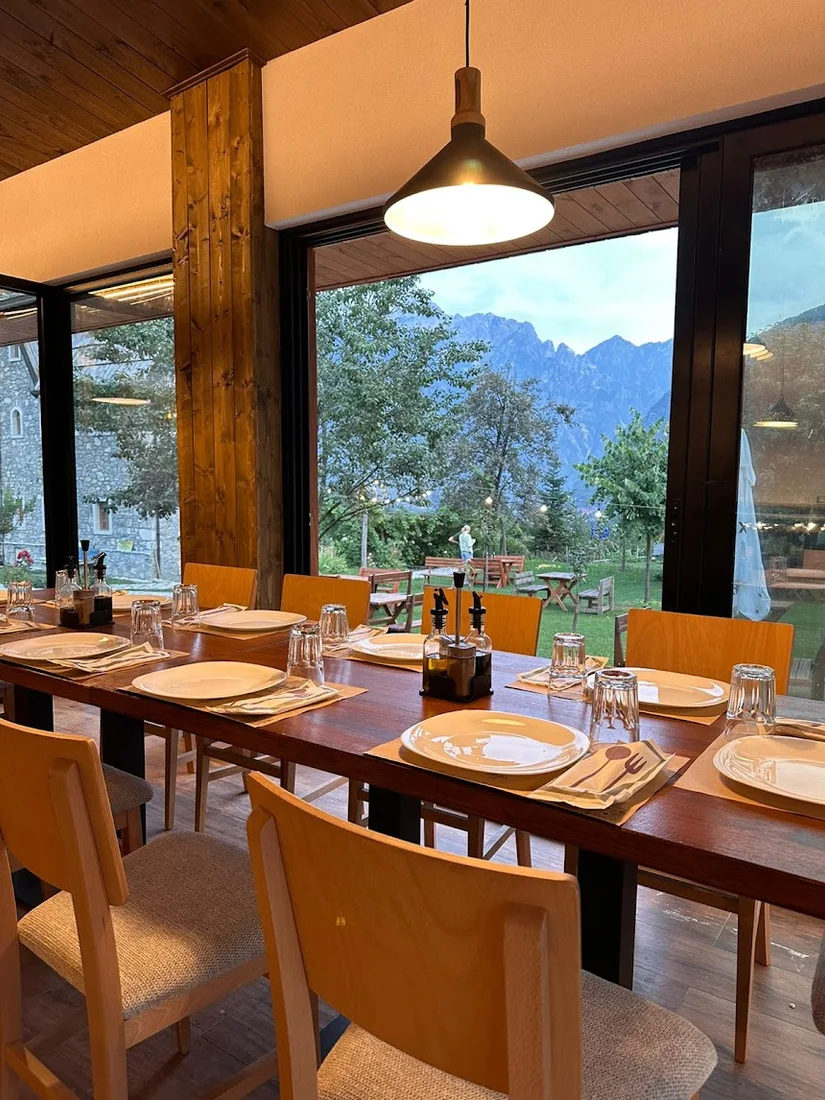 Set dining table by a picture window framing the mountains at Gjeçaj Restaurant in Theth
