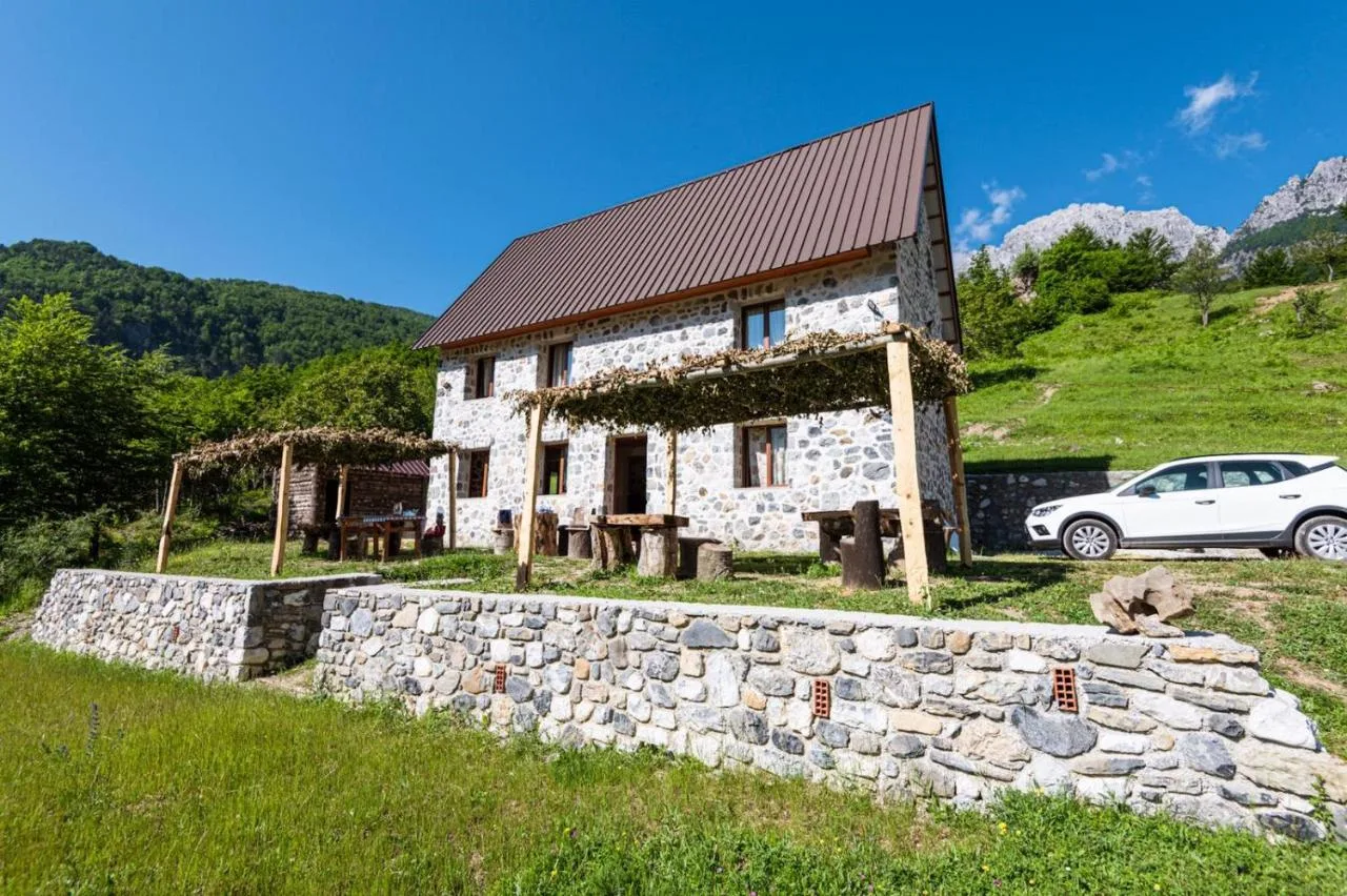 Stone house with a vine-covered timber pergola on a meadow slope at Guest House Panorama in Theth