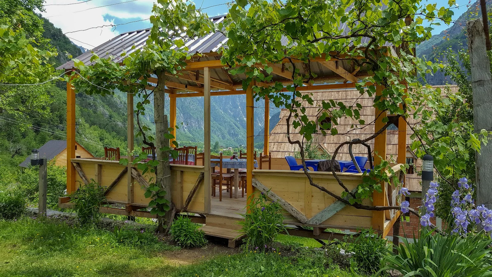 Vine-shaded wooden dining terrace with mountain views at Guesthouse Gjin Thana in Theth