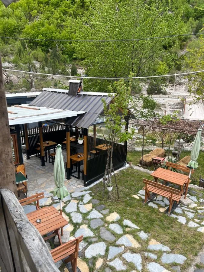 Stone-paved terrace with picnic benches and a glazed dining pavilion at Guesthouse Kujtimi in Theth