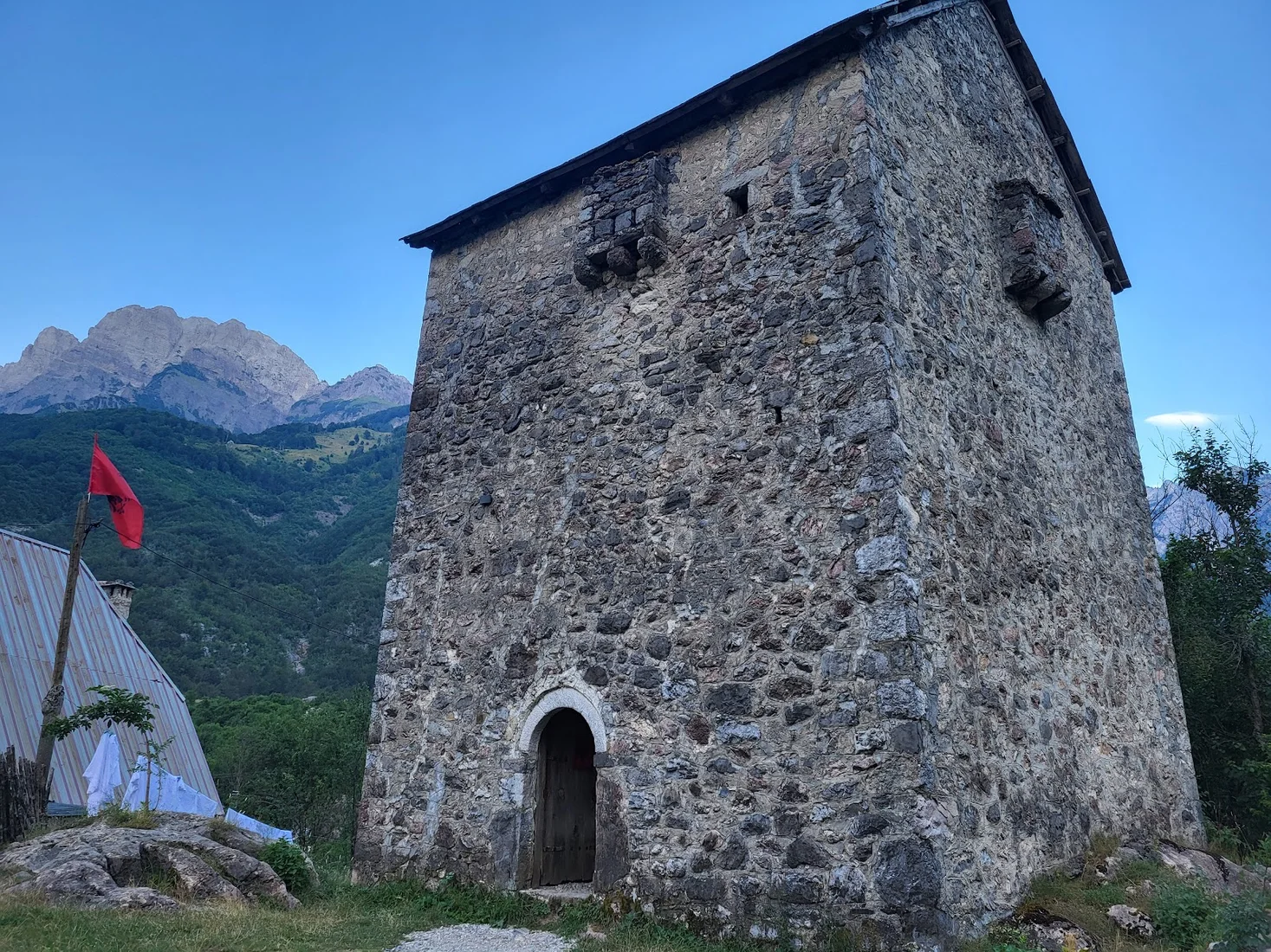 The stone Lock-in Tower of Theth with an Albanian flag and the Accursed Mountains behind