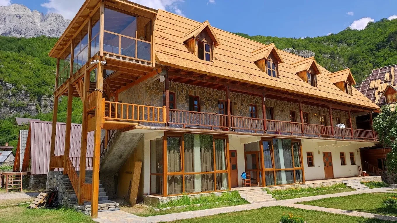 Timber-and-stone restaurant building with a glassed gallery below the peaks at Logu i Harushave in Theth