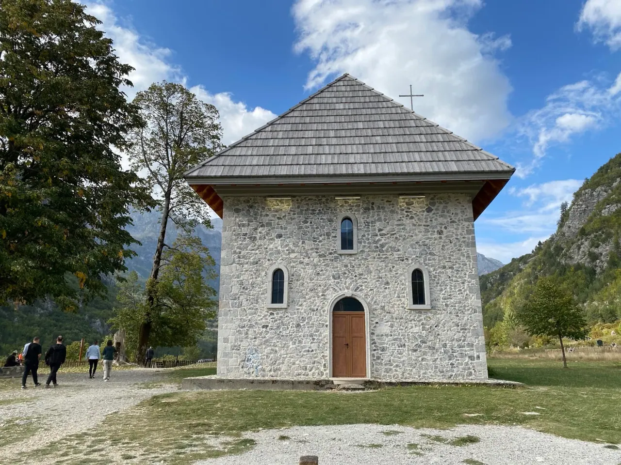 The stone church of Theth with its shingled bell tower and conical roof on a green meadow below the Albanian Alps