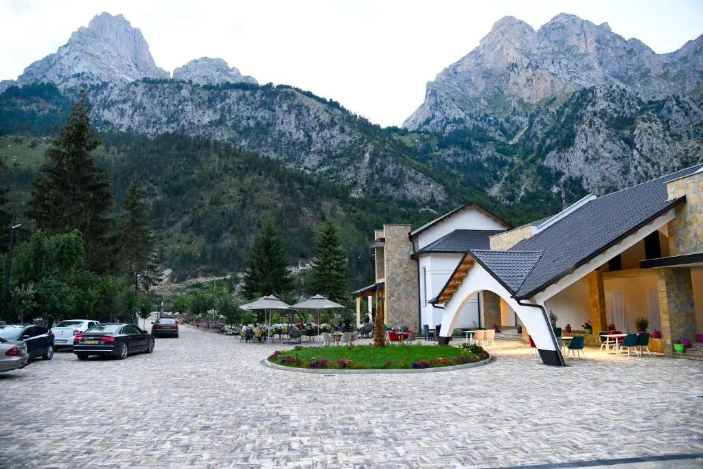 Modern stone-and-timber hotel around a paved courtyard below jagged peaks at Hotel Breezy in Valbona
