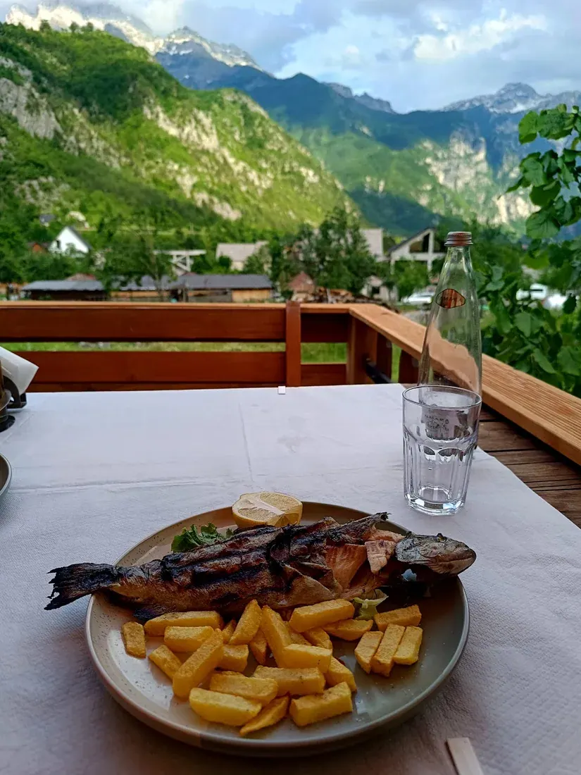 Plate of grilled river trout and chips with a valley-and-mountain view at Bar-Restaurant Jezerca in Theth
